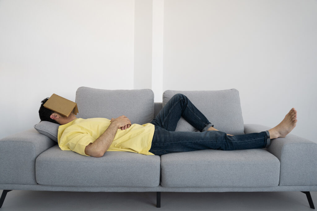 homme en train de faire la sieste sur un canapé gris avec un livre sur le visage